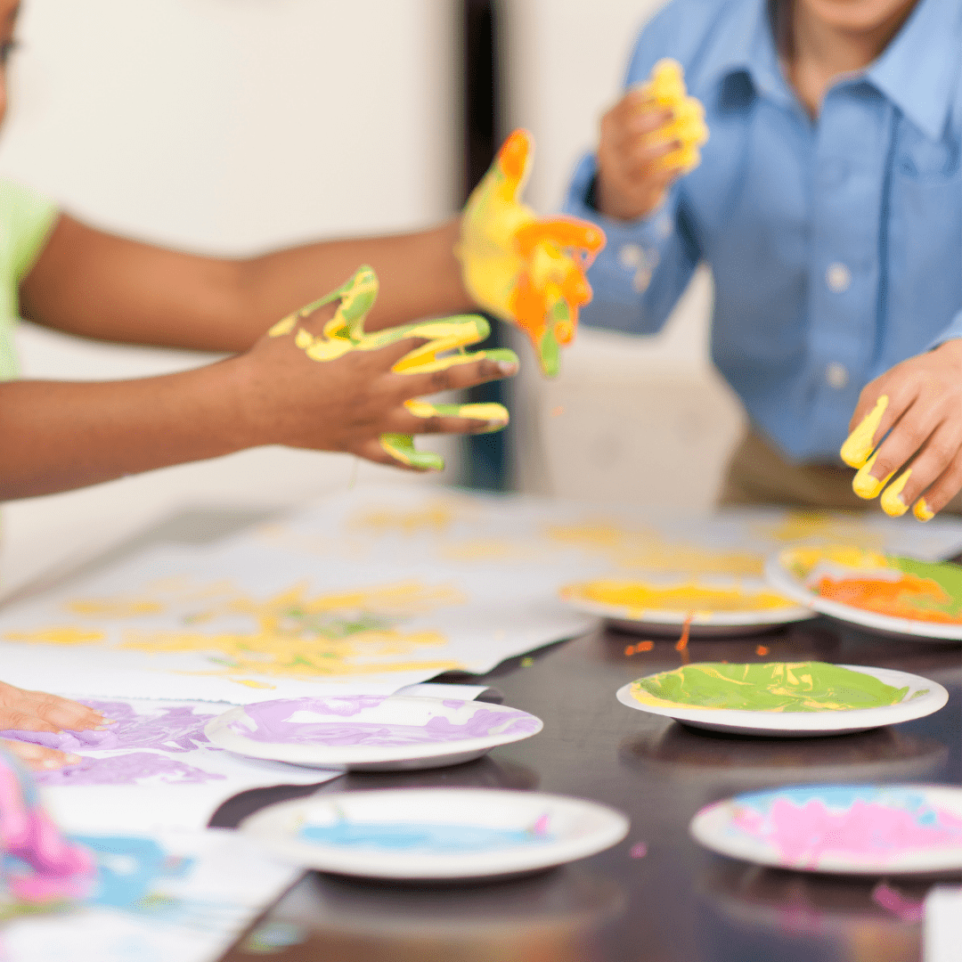 Two children making art dipping their hands in brightly coloured paint Teapot Trust art therapy
