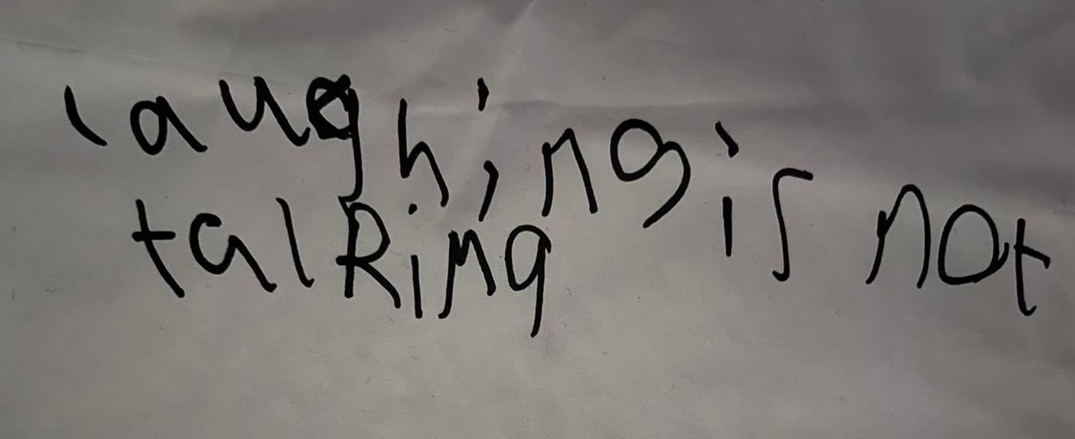White paper with black text that says 'laughing is not talking' in a child's handwriting.