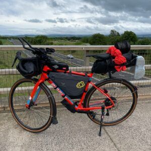 A Red Bike sits on grey tarmac packed with bags on the front and back